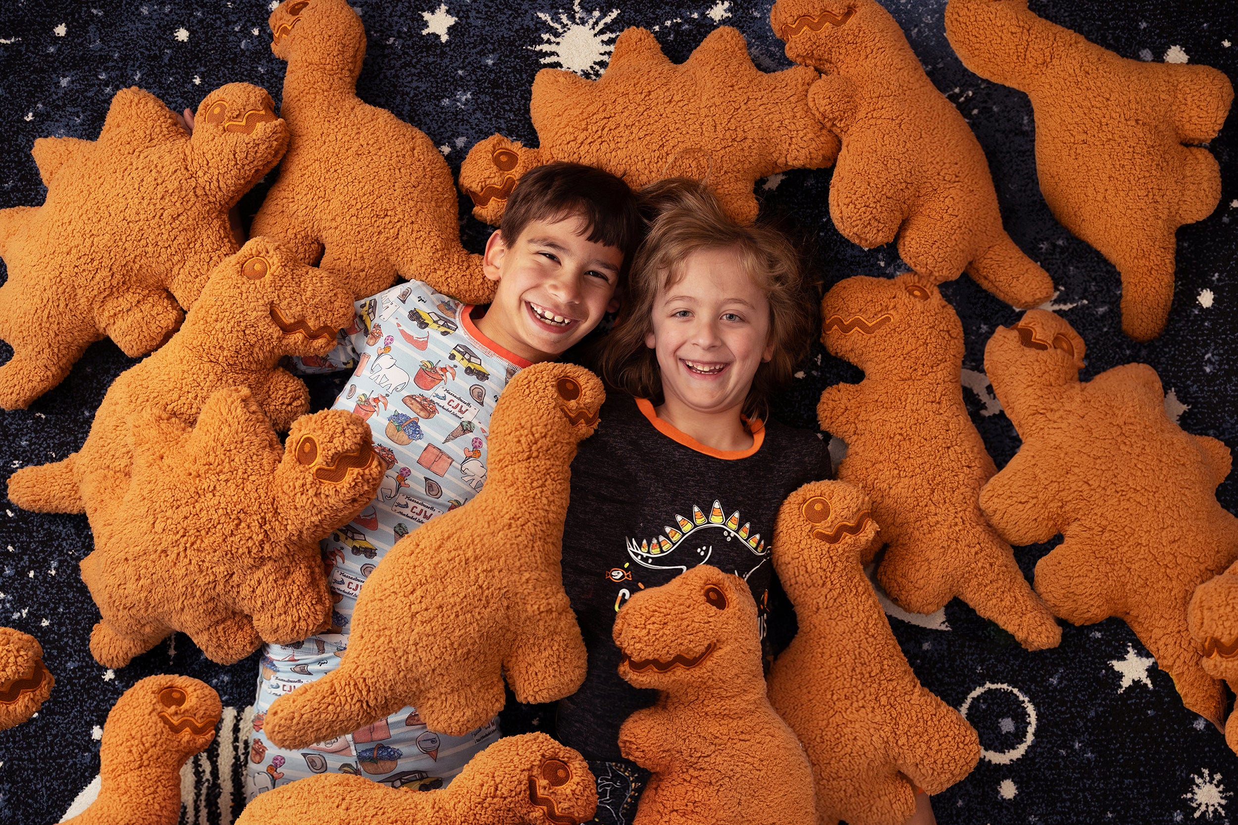 Two children surrounded by large brown dinosaur toys on a dark space-themed background